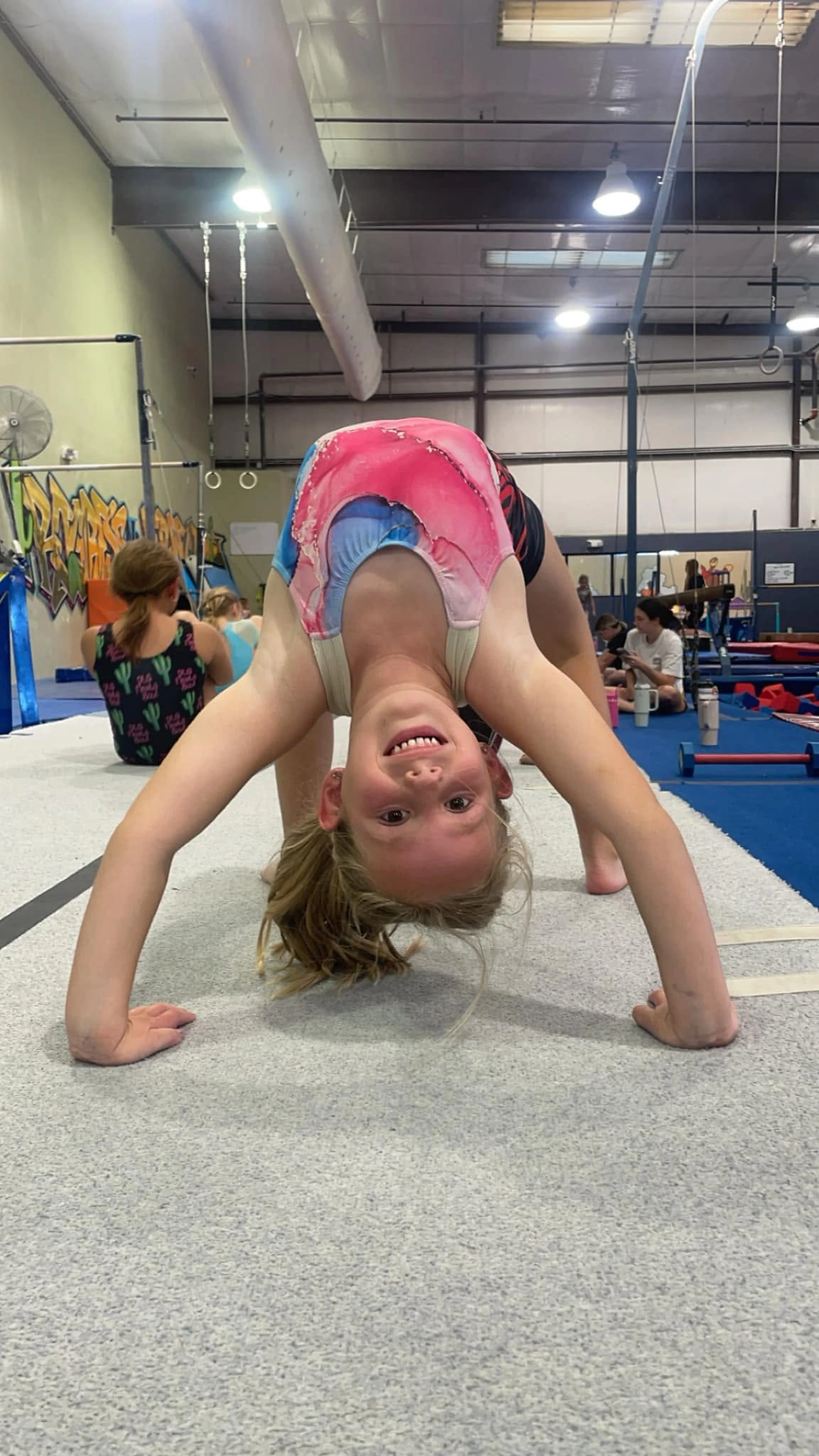 A young gymnast smiling in a backbend at Old Pueblo Gymnastics Academy